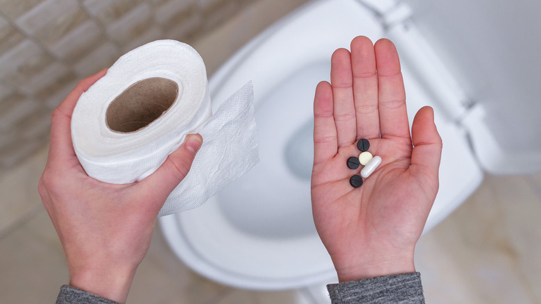 Man holding laxative pills next to toilet
