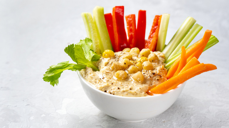 White bowl full of hummus dip and vegetable sticks