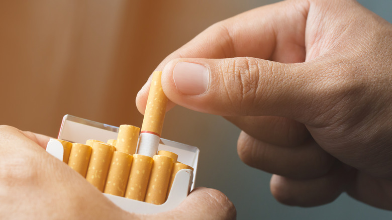 Hands pulling cigarette out of box