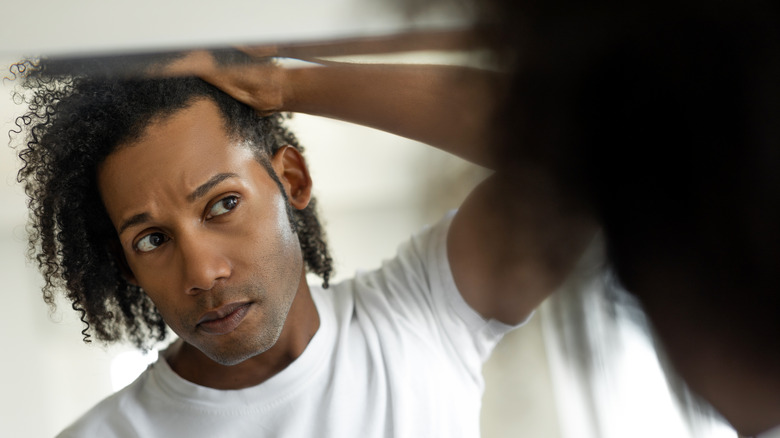 Man looking for graying hair in mirror