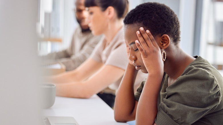 woman closing her eyes and holding her temples while at work