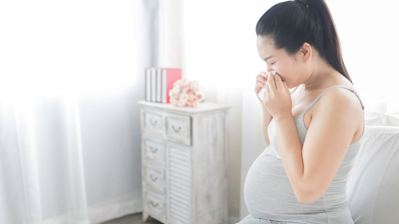 pregnant woman blowing nose in tissue