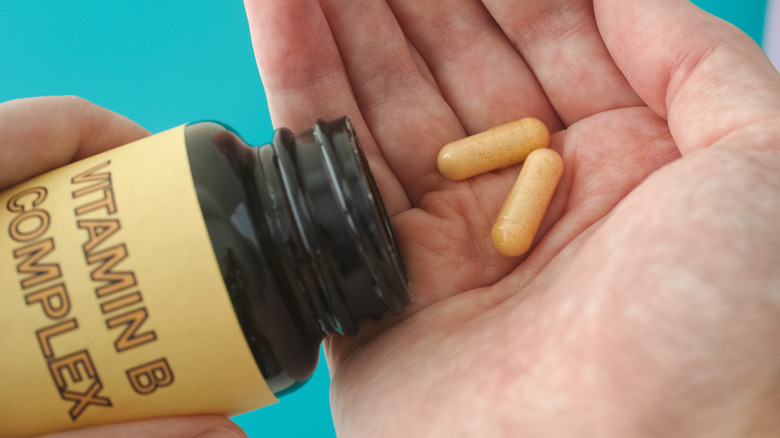 man holding vitamin b complex pills in his hand