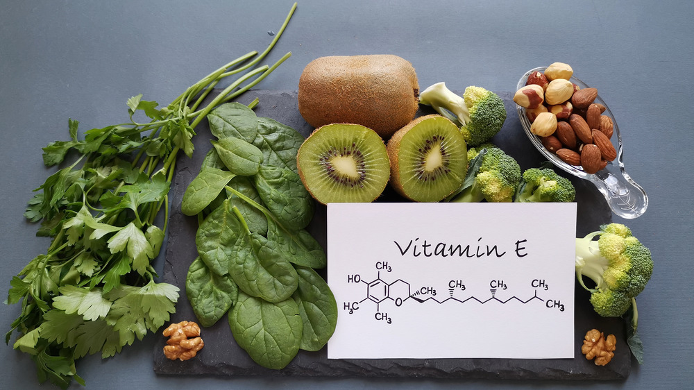 Vitamin E written on paper surrounded by leafy veggies and fruits