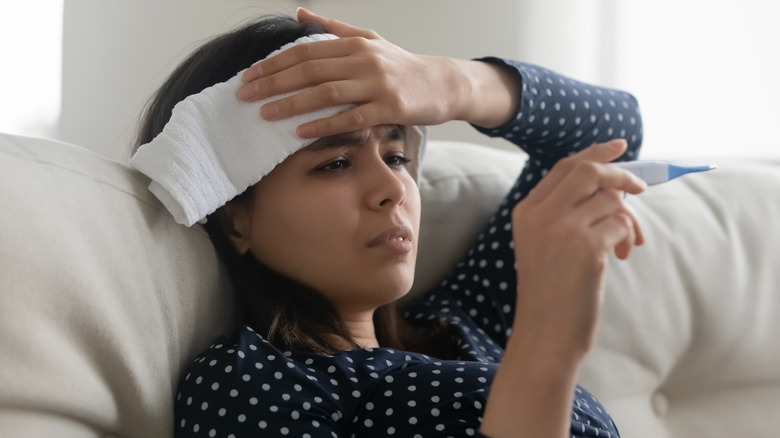 Woman with a fever looking at a thermometer