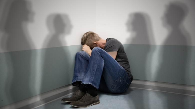 Man sitting in corner surrounded by shadows