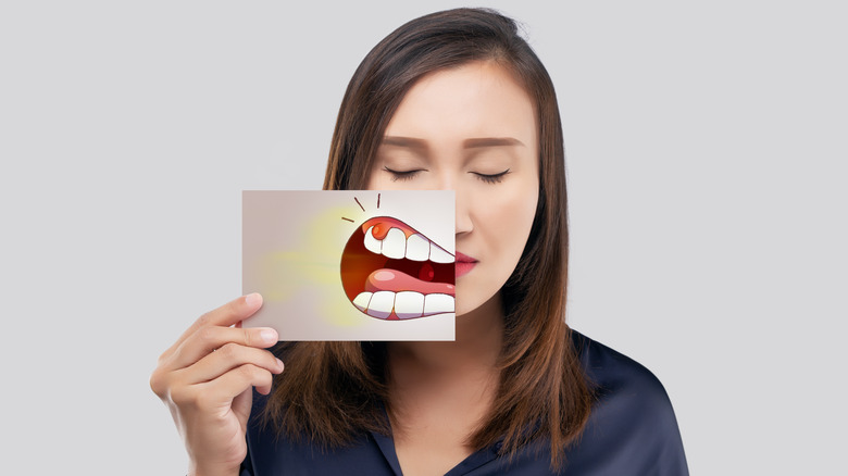 woman holding drawing of teeth in front of her face 