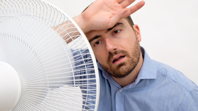 man experiencing a hot flush uses fan to cool off