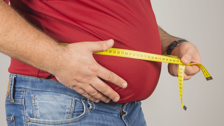 man measures belly with tape