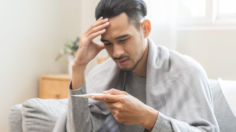 A man looking at a thermometer while touching his forehead