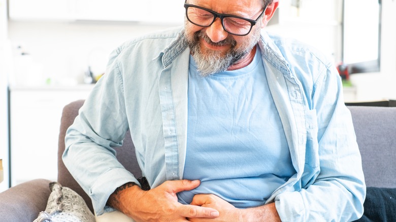 man sitting on sofa holding stomachin in pain