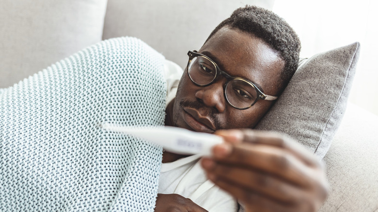 sick man in bed holding thermometer