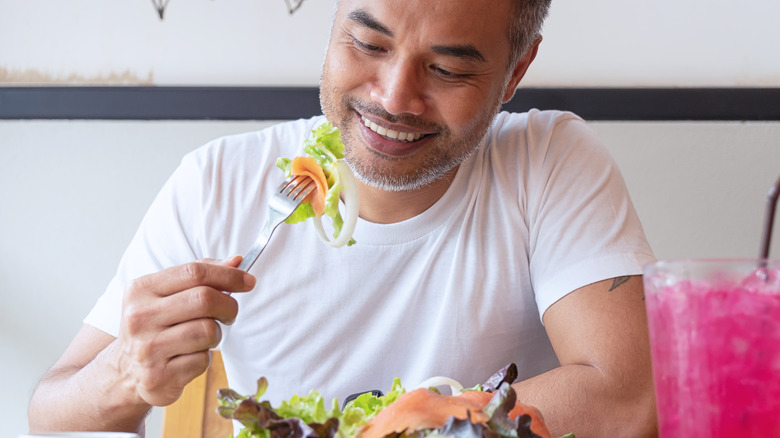 A man eating a salad with salmon on top