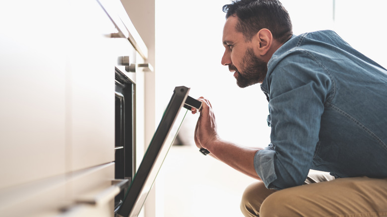 man squatting in front of the oven