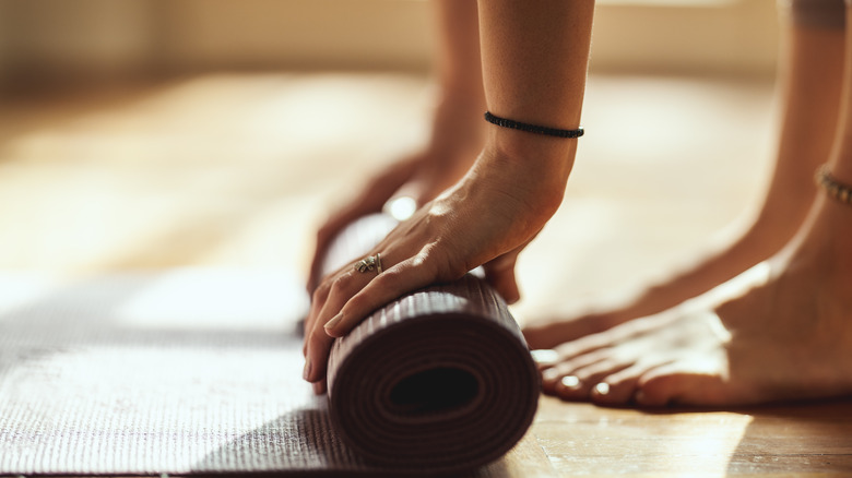 woman rolling up yoga mat at home