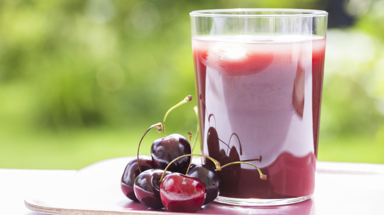 glass of tart cherry juice next to cherries