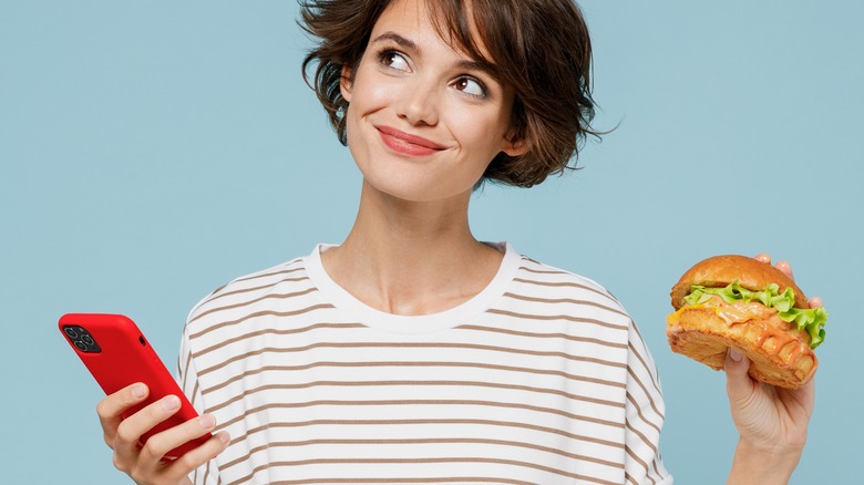 Young woman holding sandwich and phone