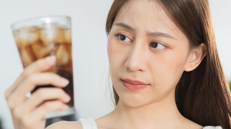 Young woman eyeing glass of soda