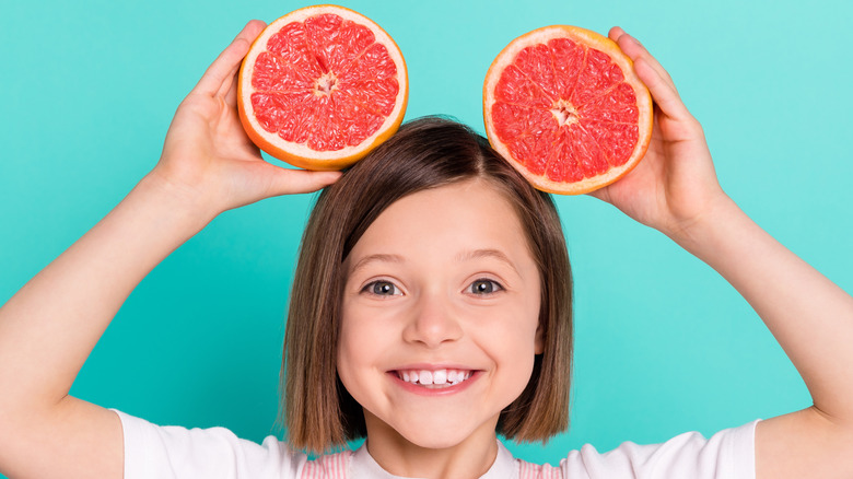 girl holding up two grapefruit halves