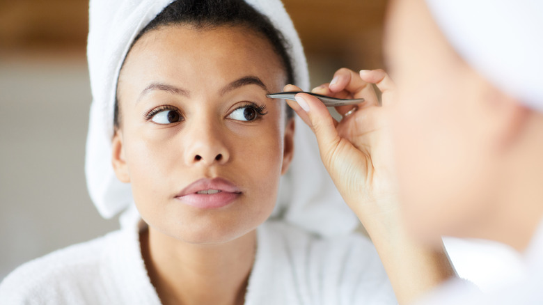 Woman using tweezers on her eyebrow