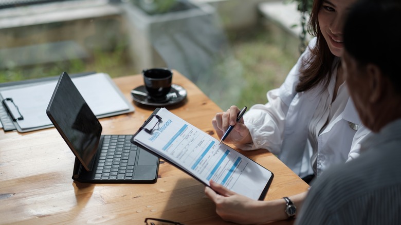 Medical employee holding health insurance sheet to patient