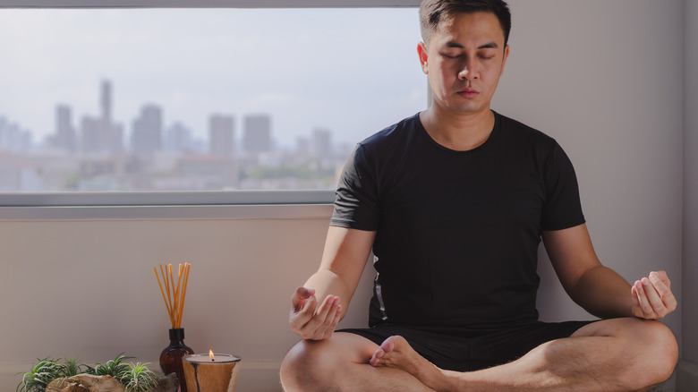 man meditating on a soft rug with candles and aromatherapy