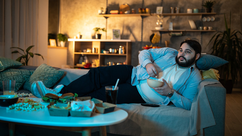 man lying on sofa, eating, watching TV