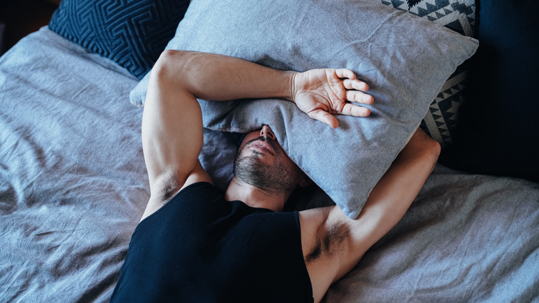 Man lying in bed with pillow over face