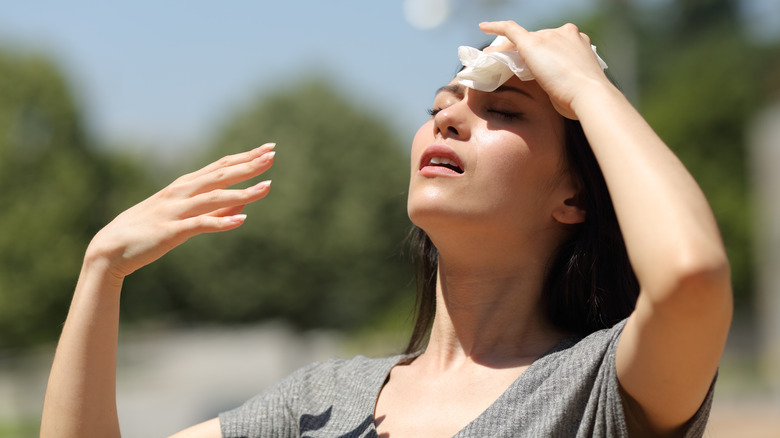 woman in sunlight sweating and blotting her forehead