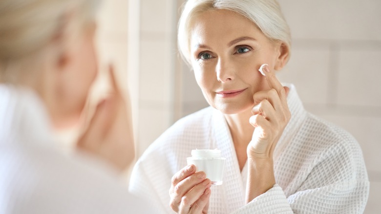 woman in robe putting cream on face