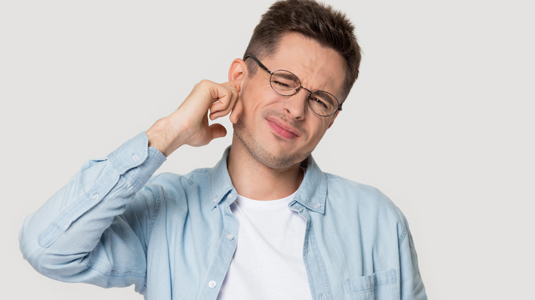 Man squinting in pain with finger to his ear