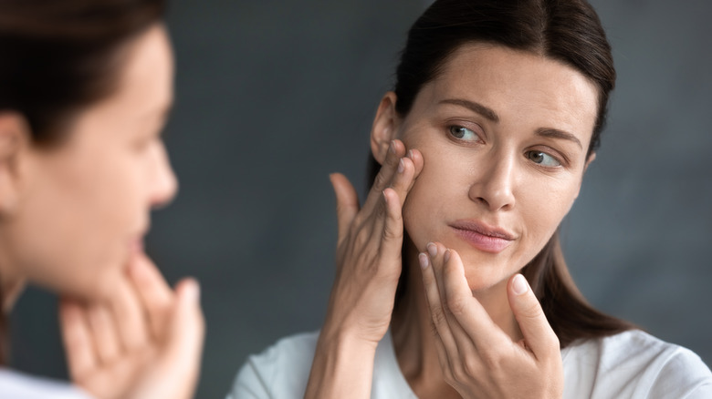 A woman looks at irritated skin on her face