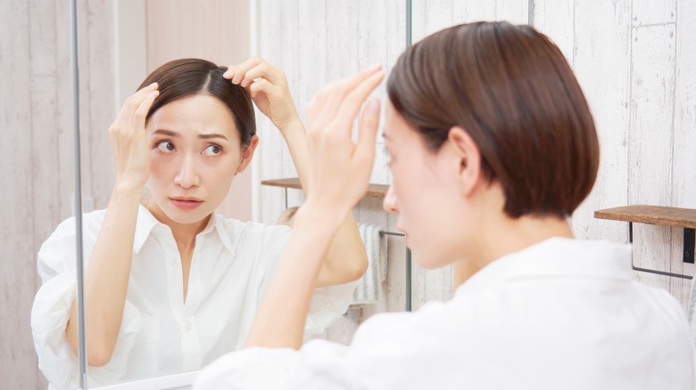 Woman lookin in mirror, touching her scalp