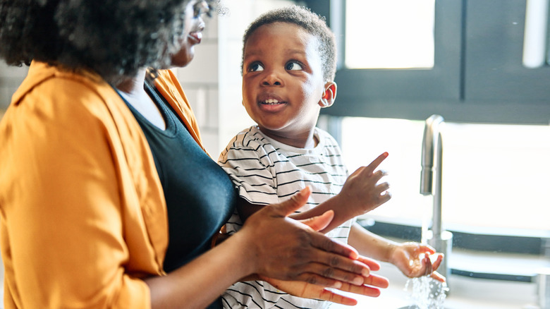 A little boy looking at his mother while washing his hands