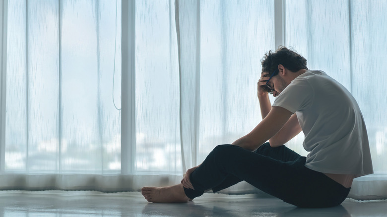 Man sits on floor with his head in his hand