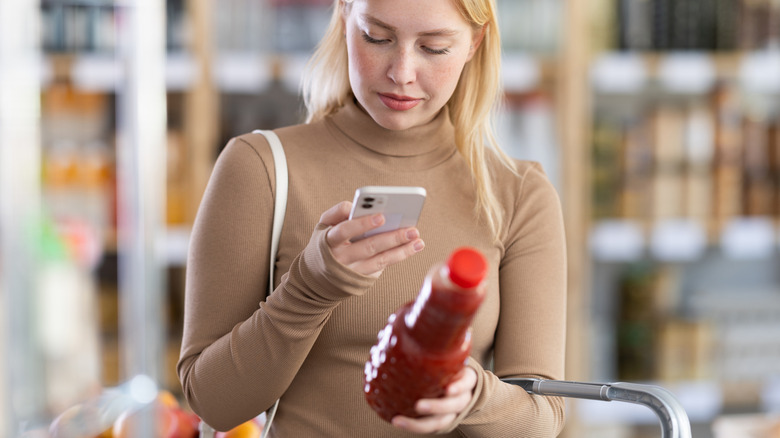 A woman holding a juice bottle looking at her phone