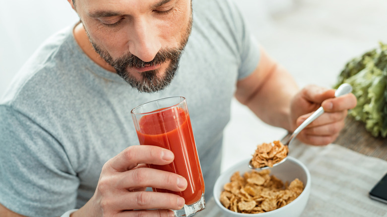 A man drinking tomato juice and eating cereal