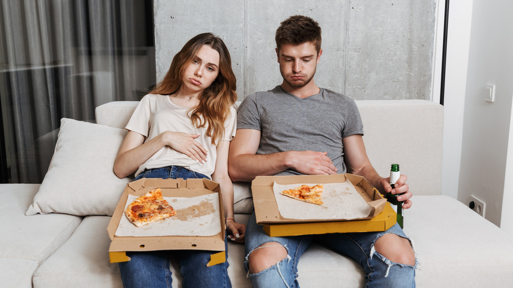 Man and woman looking stuffed after eating pizza