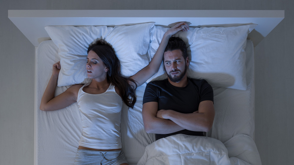 man lying awake while woman is sleeping