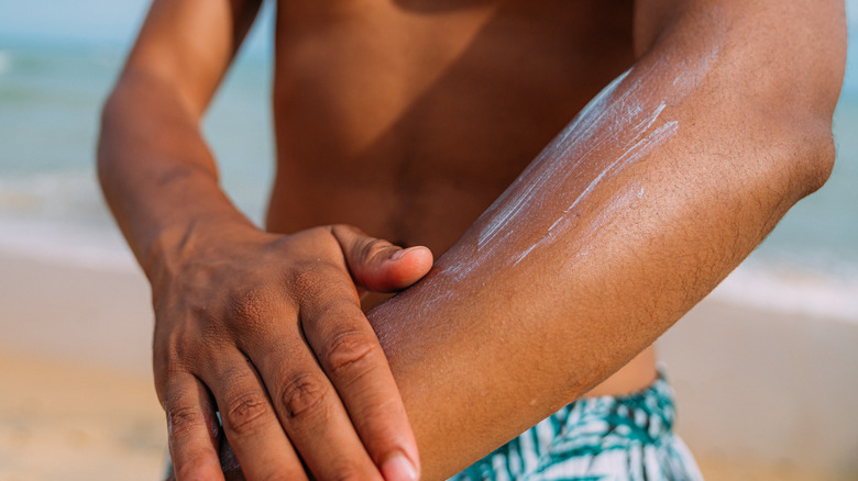 Man applies sunscreen on his arm on the beach