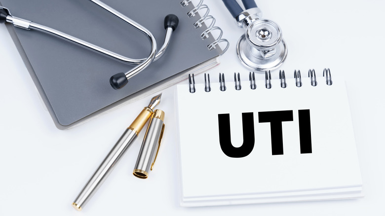Medical items on desk including a pen, stethoscope, notebook, and sign reading UTI