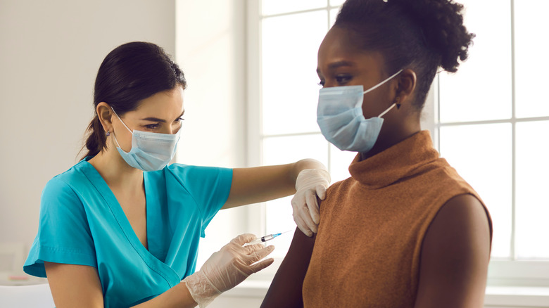 Masked woman receiving vaccine shot from masked doctor