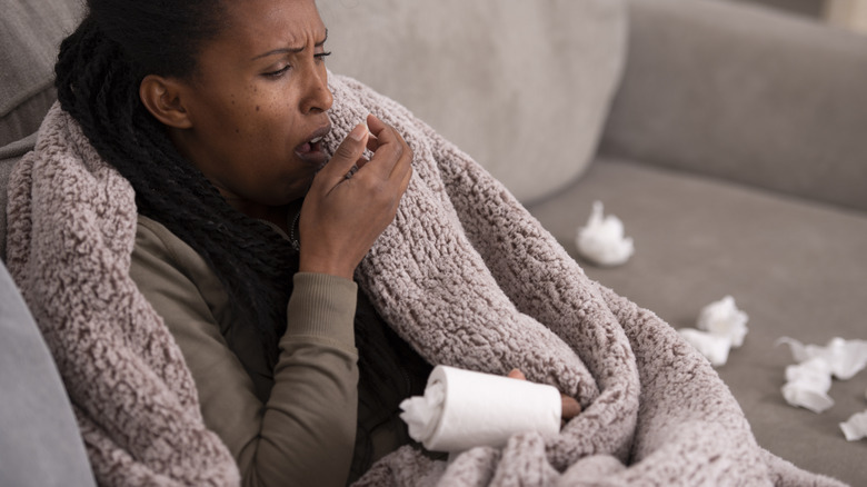 woman on couch coughing with tissues