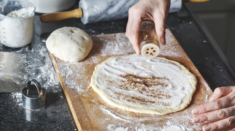 woman's hands sprinkling cinnamon to raw dough