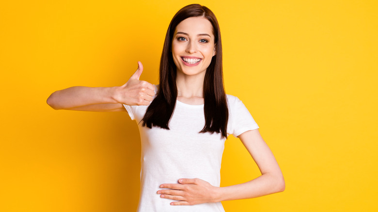 Woman with hand over stomach giving a thumbs up
