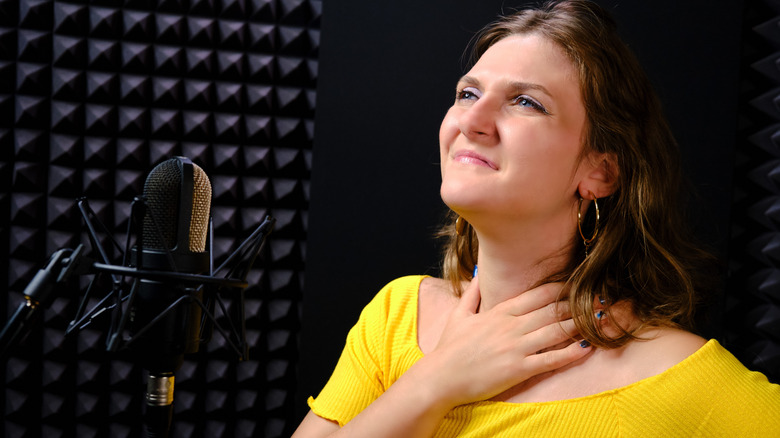 Woman in a sound recording booth holding her throat in pain