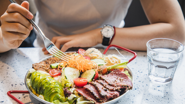 woman eating plate of salad with meat on side