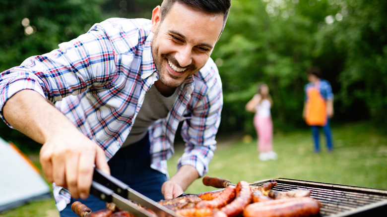 man barbequing sausages on grill outside in park