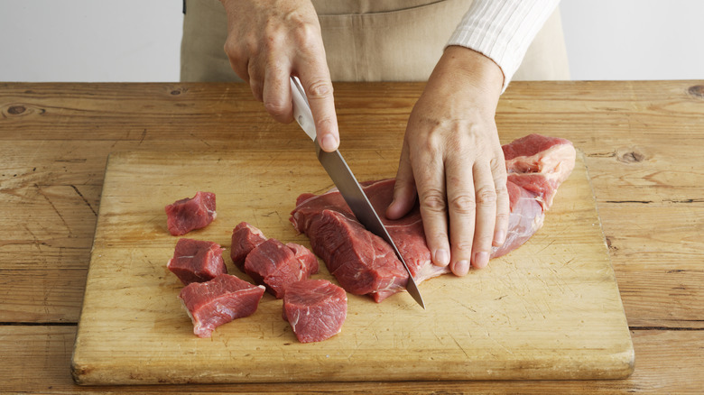 woman's hands cutting red meat on cutting board