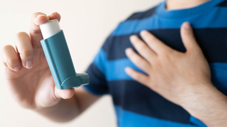 Man with hand on chest holding an inhaler in other hand